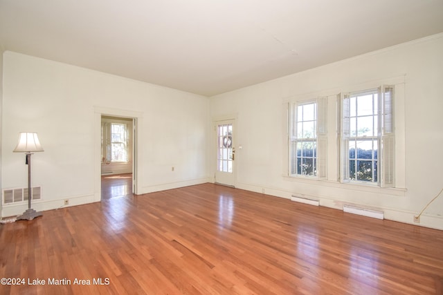 empty room featuring baseboard heating, wood-type flooring, and ornamental molding