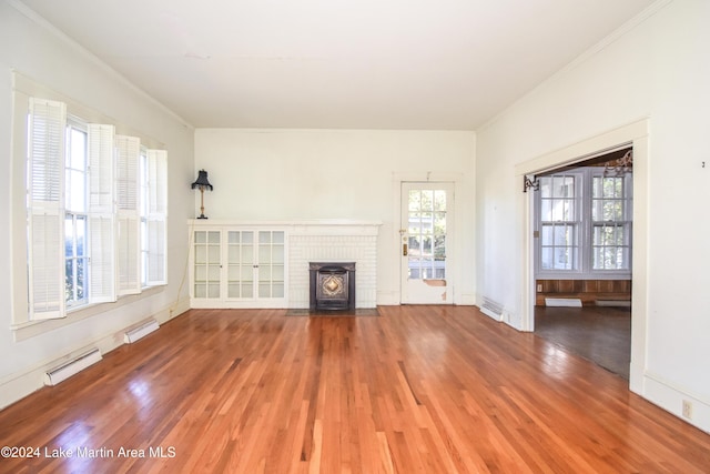 unfurnished living room featuring a wood stove, a wealth of natural light, crown molding, and hardwood / wood-style flooring