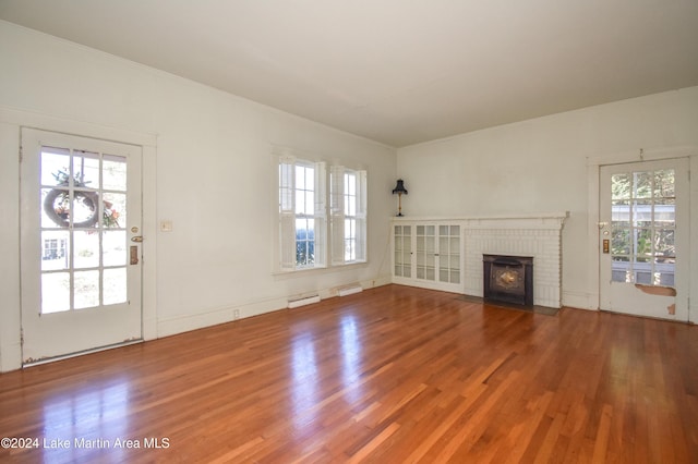 unfurnished living room featuring a fireplace, a healthy amount of sunlight, a baseboard heating unit, and hardwood / wood-style flooring