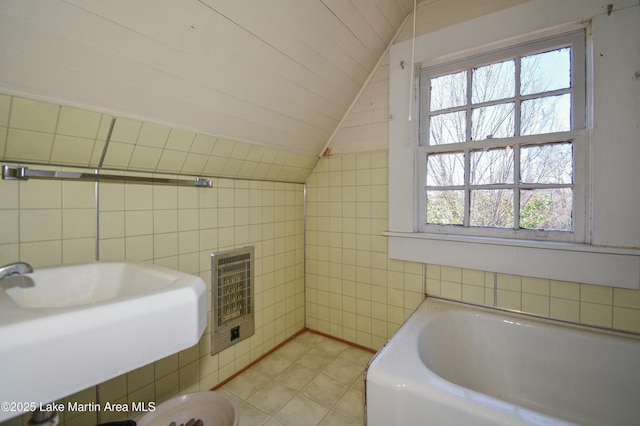 full bathroom featuring a sink, heating unit, tile walls, a bath, and vaulted ceiling