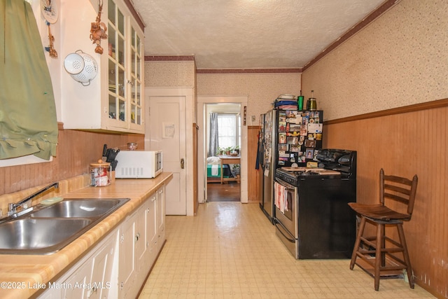 kitchen with light floors, gas range oven, wainscoting, wallpapered walls, and white microwave
