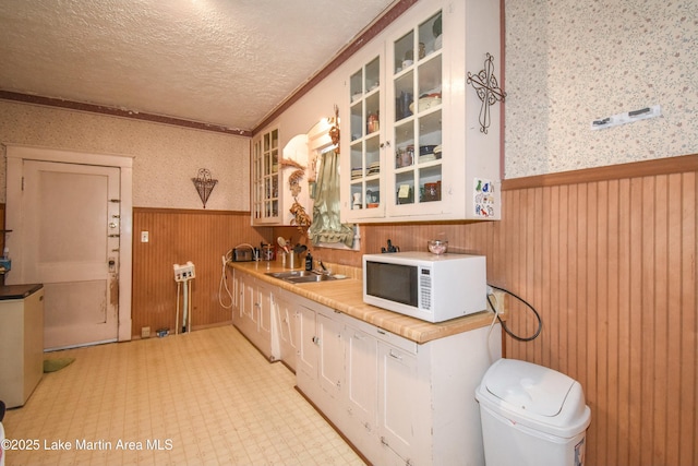 kitchen with a wainscoted wall, a sink, a textured ceiling, wallpapered walls, and white microwave