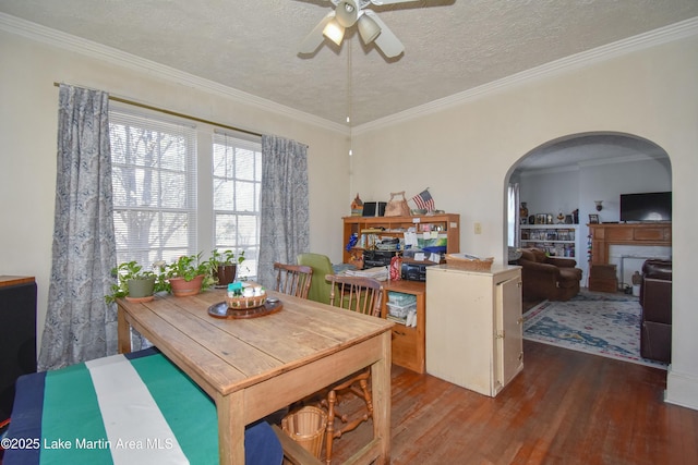 dining room featuring wood finished floors, a ceiling fan, arched walkways, a textured ceiling, and crown molding