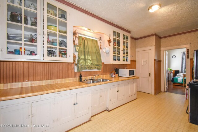 kitchen with white microwave, light floors, a sink, white cabinets, and a textured ceiling