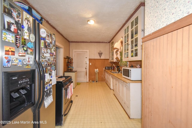 kitchen featuring ornamental molding, a textured ceiling, stainless steel appliances, glass insert cabinets, and light floors