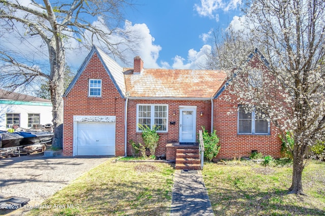tudor-style house with driveway, an attached garage, a chimney, a front lawn, and brick siding