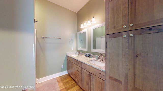 full bathroom featuring double vanity, a sink, baseboards, and wood finished floors