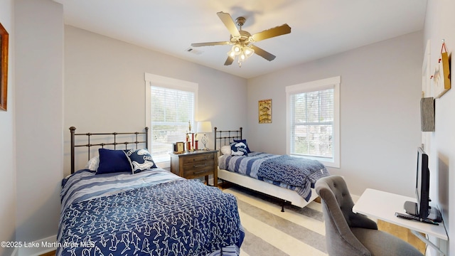carpeted bedroom with a ceiling fan, multiple windows, and visible vents
