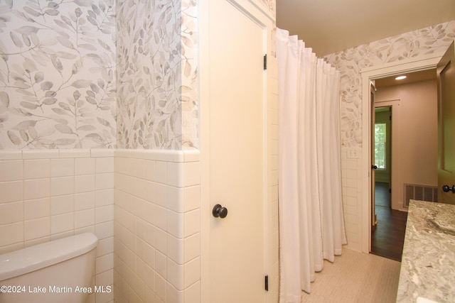 bathroom featuring hardwood / wood-style floors, tile walls, and toilet