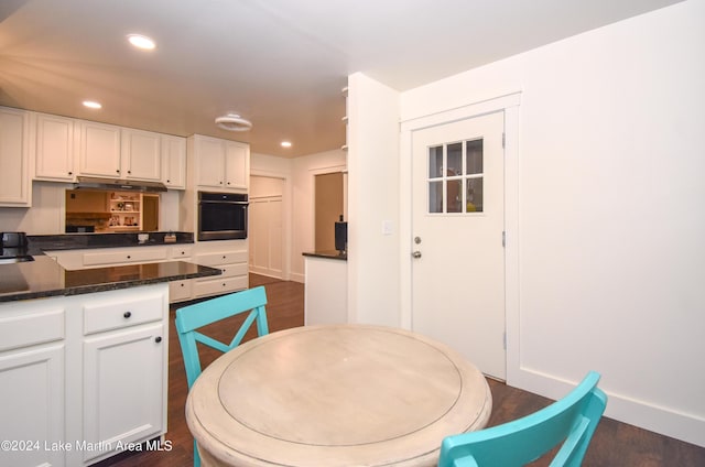 kitchen featuring black oven, dark hardwood / wood-style floors, dark stone countertops, and white cabinetry