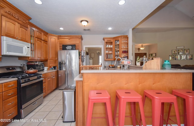 kitchen featuring appliances with stainless steel finishes, a breakfast bar area, light countertops, light tile patterned floors, and glass insert cabinets
