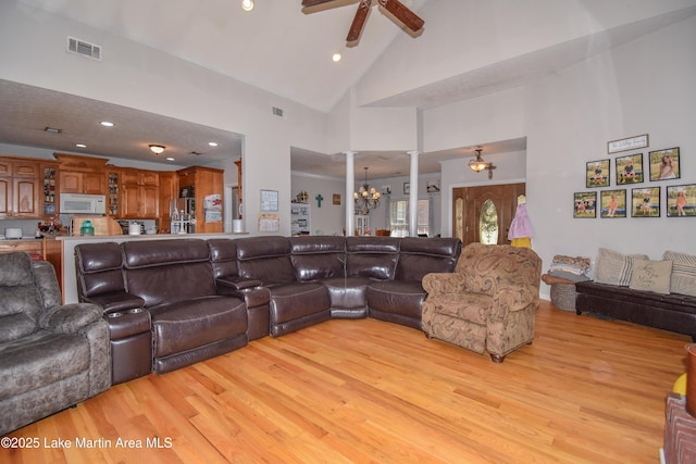 living room with ceiling fan with notable chandelier, visible vents, light wood finished floors, and high vaulted ceiling