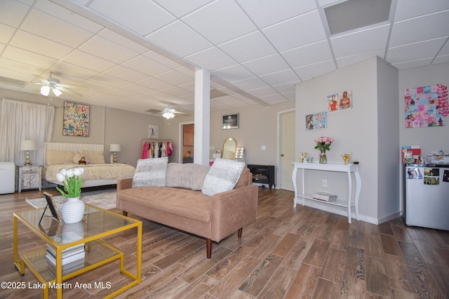 living area featuring wood finished floors, a ceiling fan, baseboards, and a drop ceiling