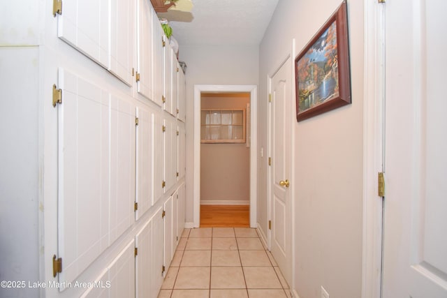 hall featuring light tile patterned floors, baseboards, and a textured ceiling