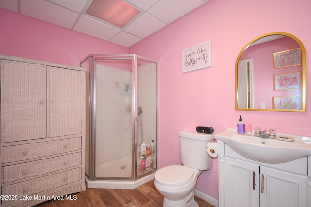 full bathroom with toilet, wood finished floors, a shower stall, a paneled ceiling, and vanity