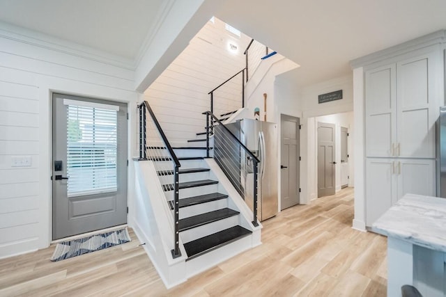 staircase featuring hardwood / wood-style floors, ornamental molding, and wood walls