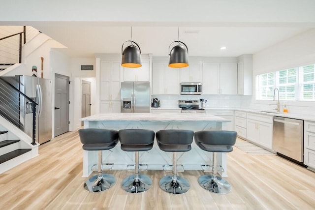 kitchen with white cabinets, sink, appliances with stainless steel finishes, decorative light fixtures, and a kitchen island