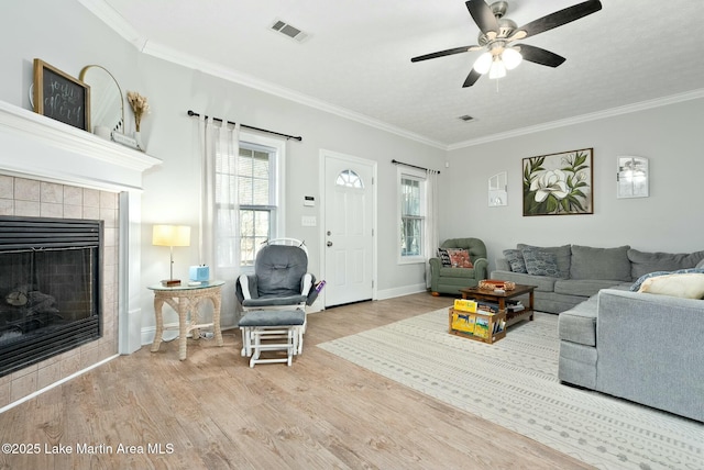 living room with light wood-type flooring, ceiling fan, crown molding, and a tiled fireplace