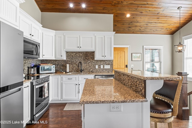 kitchen featuring a breakfast bar area, a sink, appliances with stainless steel finishes, wooden ceiling, and dark wood finished floors