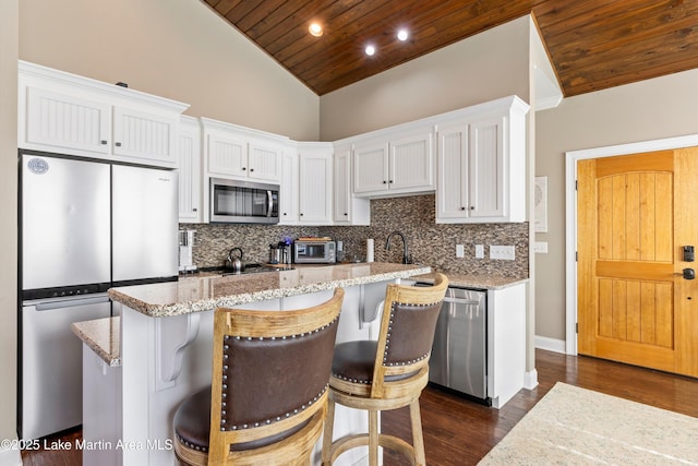 kitchen featuring a breakfast bar, stainless steel appliances, white cabinetry, and wood ceiling