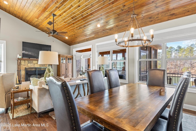 dining space with wooden ceiling, wood-type flooring, a stone fireplace, vaulted ceiling, and ceiling fan with notable chandelier