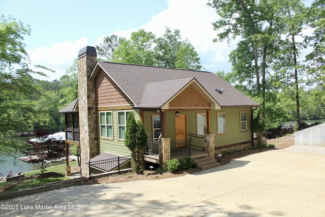 view of front of house featuring a chimney, a porch, a shingled roof, and a water view