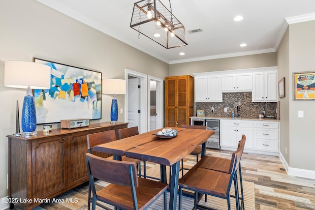 dining area featuring sink, an inviting chandelier, wine cooler, ornamental molding, and light wood-type flooring