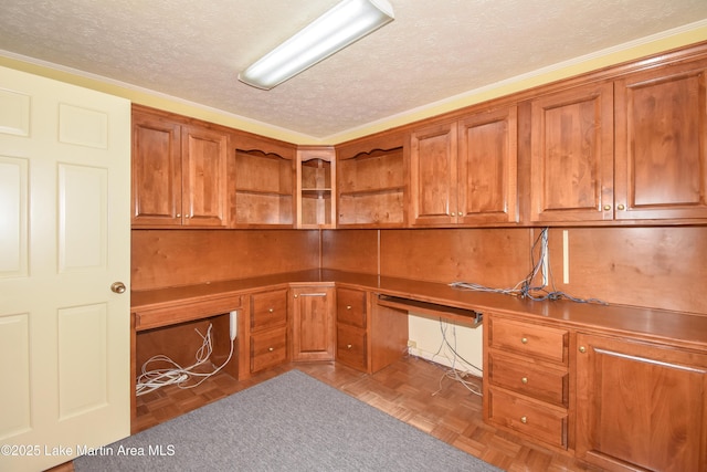 unfurnished office featuring a textured ceiling, built in desk, and parquet floors