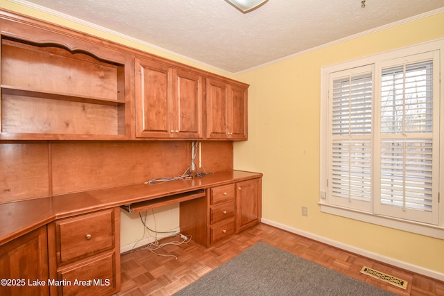 unfurnished office with built in desk, light parquet floors, a textured ceiling, and ornamental molding