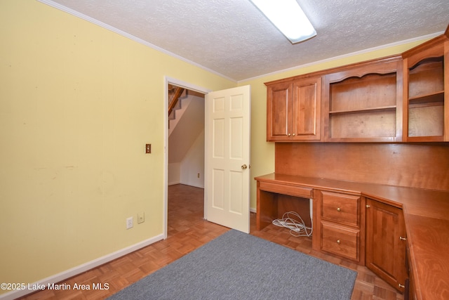 unfurnished office featuring a textured ceiling, ornamental molding, parquet floors, and built in desk