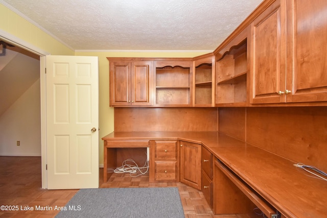 unfurnished office featuring a textured ceiling, crown molding, built in desk, and light parquet flooring