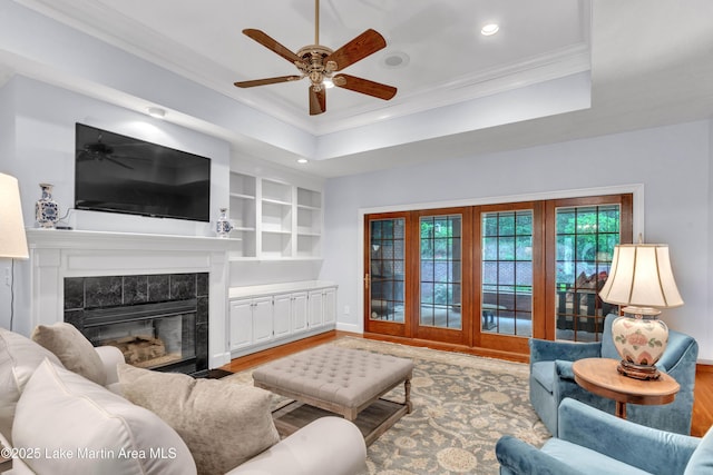living room featuring a ceiling fan, a tile fireplace, light wood-style flooring, crown molding, and recessed lighting