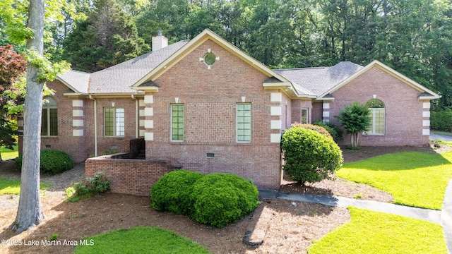 view of front of home with brick siding, a chimney, a front yard, crawl space, and roof with shingles
