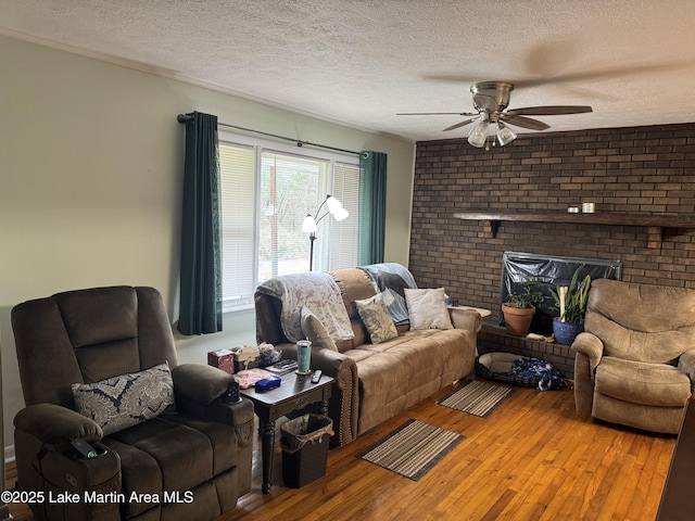 living room with ceiling fan, hardwood / wood-style floors, a textured ceiling, and a brick fireplace