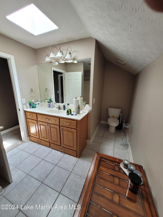 bathroom with vanity, tile patterned flooring, vaulted ceiling with skylight, toilet, and a textured ceiling