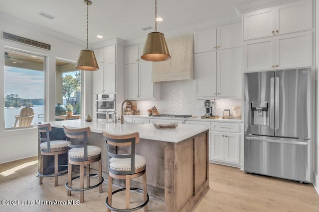 kitchen featuring white cabinetry, pendant lighting, a kitchen island with sink, a water view, and appliances with stainless steel finishes