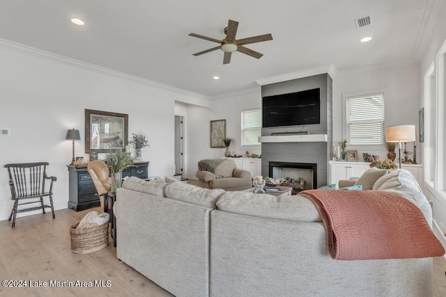 living room featuring a large fireplace, light hardwood / wood-style floors, ceiling fan, and ornamental molding