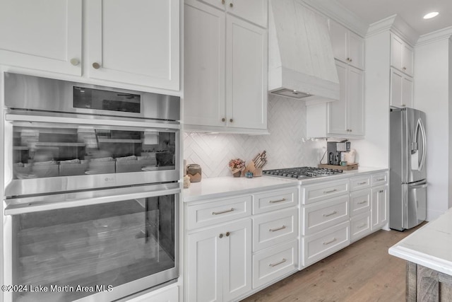 kitchen with premium range hood, decorative backsplash, appliances with stainless steel finishes, light hardwood / wood-style floors, and white cabinetry