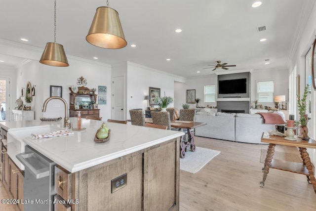 kitchen with light wood-type flooring, ceiling fan, sink, pendant lighting, and a center island with sink