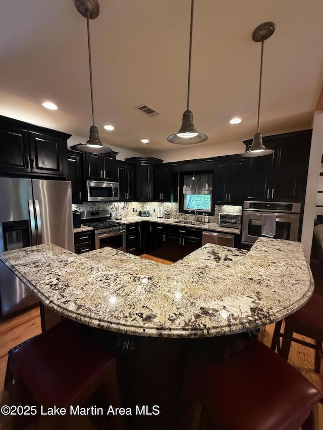 43 Shady Cv, Dadeville, AL 36853 - kitchen with stainless steel appliances, dark cabinetry, a breakfast bar area, light stone counters, and decorative backsplash