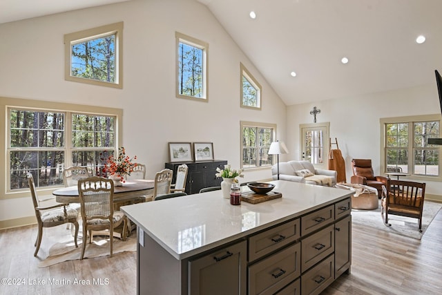 kitchen with a center island, light stone countertops, light wood-type flooring, and high vaulted ceiling