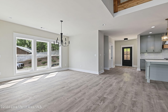 unfurnished living room featuring light hardwood / wood-style flooring, a healthy amount of sunlight, and a notable chandelier