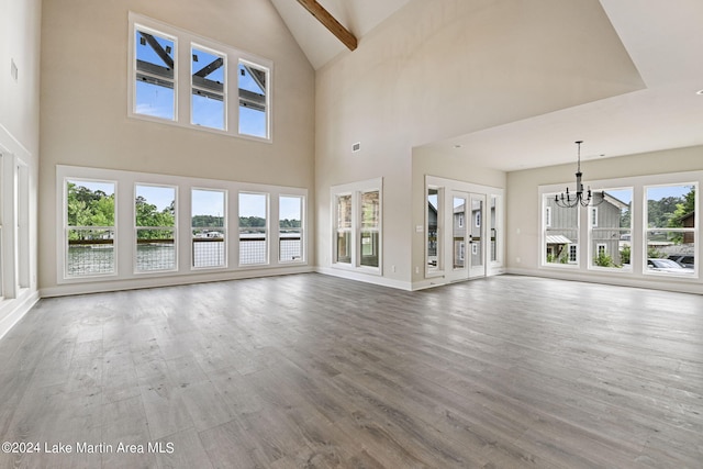 unfurnished living room with a wealth of natural light, an inviting chandelier, high vaulted ceiling, and hardwood / wood-style flooring