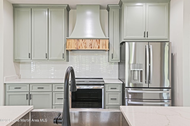 kitchen featuring custom exhaust hood, stainless steel fridge, light stone countertops, and decorative backsplash