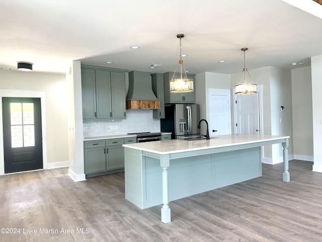 kitchen featuring premium range hood, stainless steel appliances, sink, pendant lighting, and light hardwood / wood-style floors