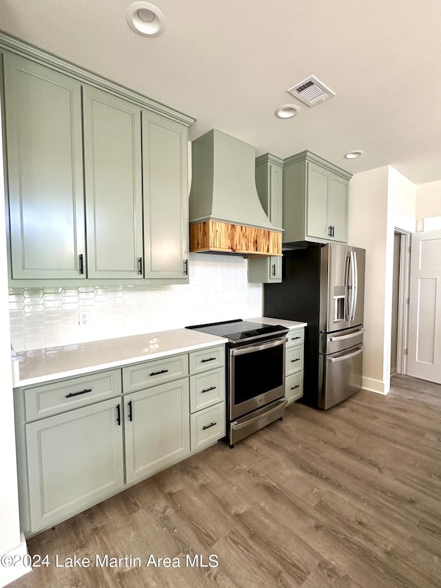 kitchen featuring light wood-type flooring, tasteful backsplash, custom range hood, stainless steel appliances, and green cabinets