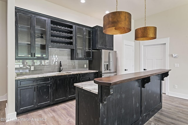 kitchen featuring sink, stainless steel refrigerator with ice dispenser, hanging light fixtures, light hardwood / wood-style flooring, and butcher block countertops