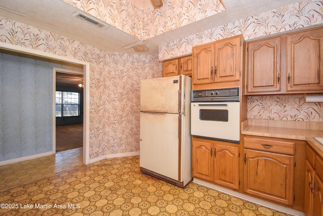 405 4th St, Tallassee, AL 36078 - kitchen featuring white appliances, wallpapered walls, light countertops, brown cabinets, and light floors