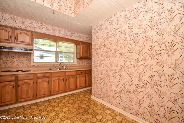 405 4th St, Tallassee, AL 36078 - kitchen with wallpapered walls, under cabinet range hood, light countertops, brown cabinetry, and white stovetop