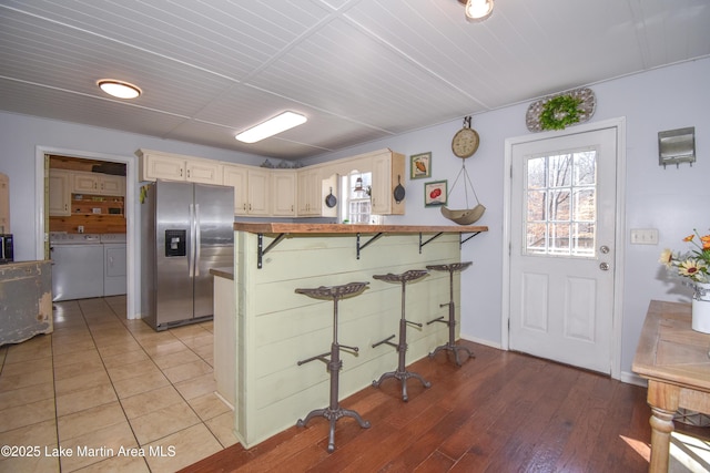 kitchen with washer and clothes dryer, stainless steel fridge, light hardwood / wood-style floors, a kitchen bar, and kitchen peninsula